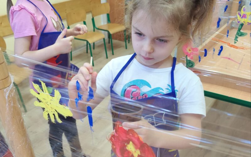 Skupiona dziewczynka maluje na folii.